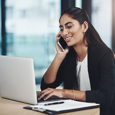 India woman talking on a mobile while typing on her laptop